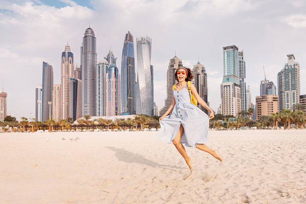 Funny woman in a sundress jumping with a background of huge skyscrapers in Dubai - Foto, imagen