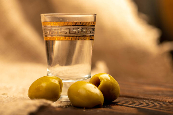 Ein Glas Wodka und gesalzene Oliven auf einem hausgemachten Stoff mit rauer Konsistenz. Selektive Fokussierung aus nächster Nähe - Foto, Bild