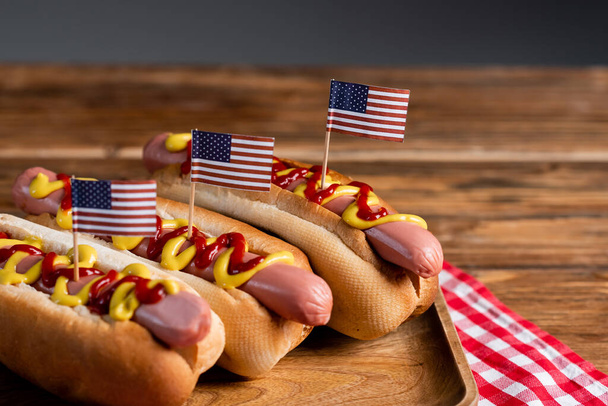 tasty hot dogs with sauces and small usa flags on wooden surface isolated on grey - Фото, зображення