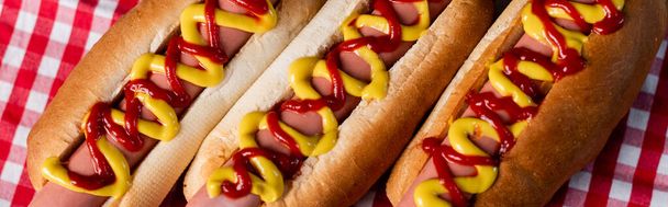 close up view of tasty hot dogs with mustard and ketchup on plaid tablecloth, banner - Photo, Image