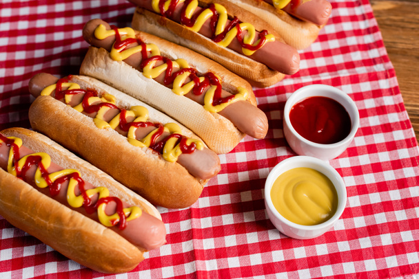 delicious hot dogs near ketchup and mustard on checkered napkin and wooden table - Φωτογραφία, εικόνα