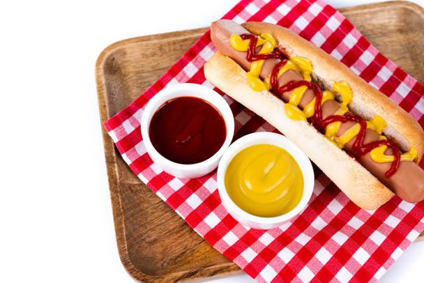 tasty hot dog with mustard and ketchup on plaid table napkin and wooden tray isolated on white - Photo, Image
