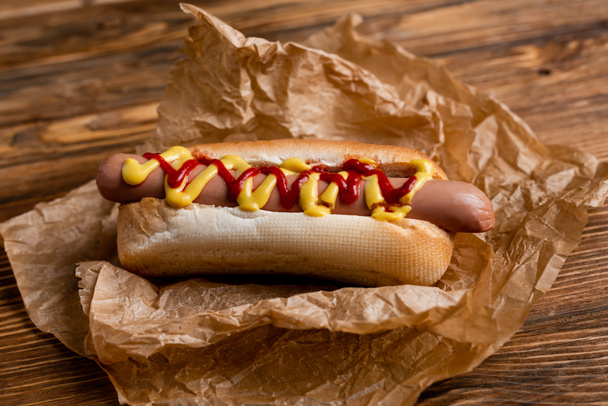 close up view of hot dog with ketchup and mustard and crumpled paper on wooden table - Foto, imagen