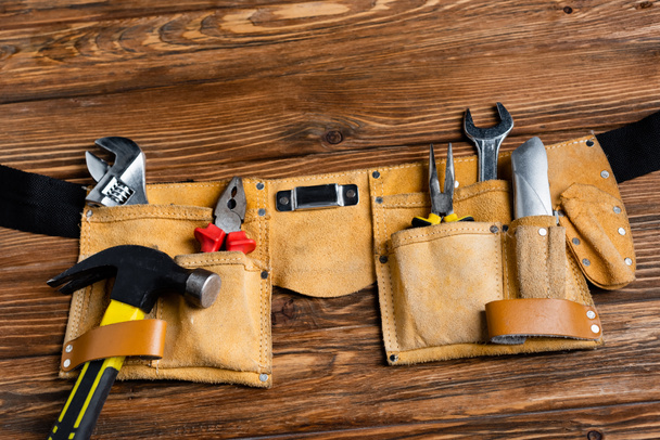 top view of leather tool belt with hammer, pliers, knife and wrenches on wooden table, labor day concept - Photo, Image