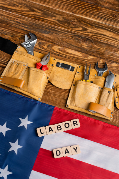 pohled shora na kostky s nápisy ze dne práce, vlajku USA a pás s nářadím s různými nástroji na dřevěném stole - Fotografie, Obrázek