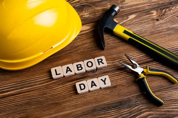 helmet, hammer, pliers and cubes with labor day lettering on wooden surface - Photo, Image