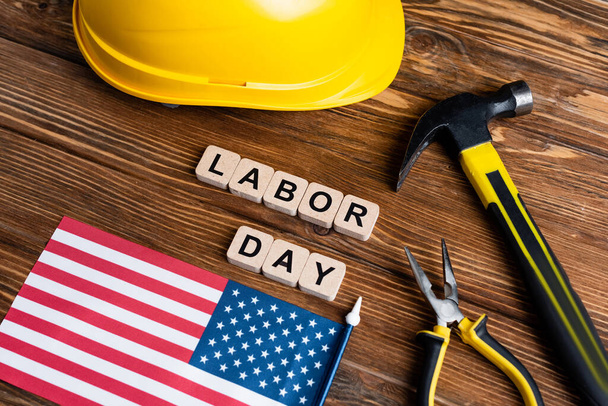 usa flag, hammer, pliers, hardhat and cubes with labor day lettering on wooden table - Foto, immagini