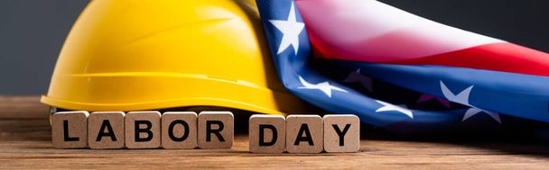 cubes with labor day lettering near helmet and usa flag on wooden surface isolated on grey, banner - Photo, Image