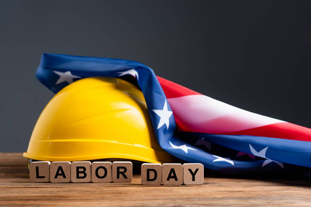cubes with labor day lettering near hardhat and usa flag on wooden surface isolated on grey - Foto, Imagem