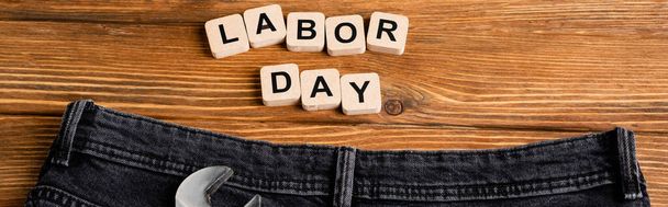 top view of wrench and jeans near cubes with labor day lettering on wooden table, banner - Foto, Imagem