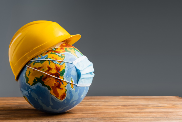medical mask and hardhat on globe on wooden surface isolated on grey, labor day concept - Photo, Image