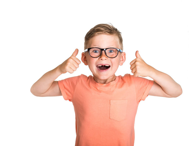 Портрет счастливого мальчика, показывающего большие пальцы на белом фоне. Возвращайся в школу. Блондинка в очках с открытым ртом. Веснушчатое лицо с молоком или выпавшим временным зубом - Фото, изображение