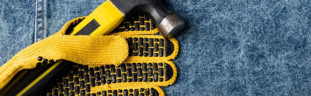верхний вид молотка рядом с желтой резинкой рабочая перчатка на джинсовой ткани, концепция трудового дня, баннер - Фото, изображение