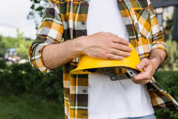 partial view of builder in plaid shirt holding helmet outdoors, labor day concept - Photo, Image
