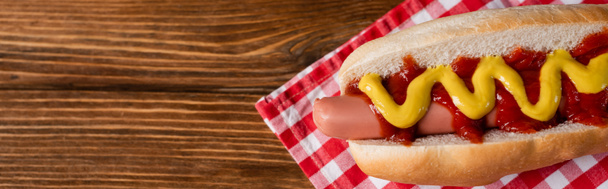 top view of tasty hot dog with sauces on checkered napkin and wooden table, banner - Foto, afbeelding