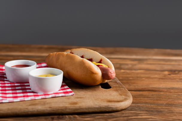 κοπής σκάφους με hot dog, κέτσαπ και μουστάρδα σε μπολ σε ξύλινο τραπέζι απομονώνονται σε γκρι - Φωτογραφία, εικόνα