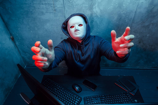 Anonymous hacker wearing face mask working on computer in dark room - Zdjęcie, obraz