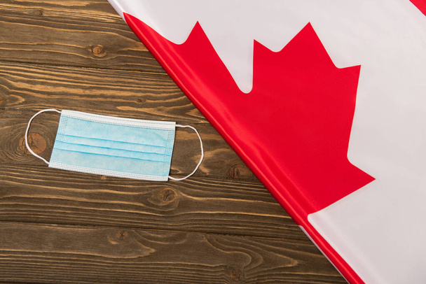bovenaanzicht van de Canadese vlag en medisch masker op houten oppervlak, covid-19 concept  - Foto, afbeelding