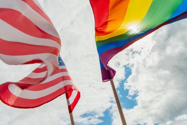 onderaanzicht van Amerikaanse en kleurrijke lgbt vlaggen tegen de lucht met wolken - Foto, afbeelding