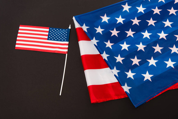 small american flag near fabric with stars and stripes isolated on black - Fotoğraf, Görsel
