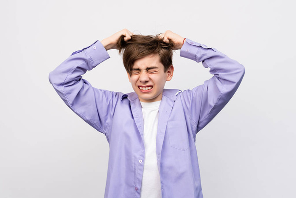Frustrated boy with eyes closed, messing up and pulling his hair, hands to head shouting and screaming, isolated over light gray background. Stressed adolescent, failure concept - Photo, Image