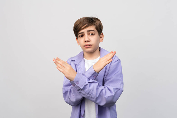 Stop, no way. Serious boy shows stop prohibit gesture with cross hands, keep your distance, standing displeased against light gray background - Photo, Image
