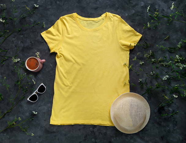 Желтая простая футболка имитирует чашку кофе на темном фоне. Бланшированная хлопковая рубашка соблазняет креативным дизайном. Женщина освещает летние солнцезащитные очки соломенной шляпной одеждой. Случайная одежда для социальных сетей. - Фото, изображение
