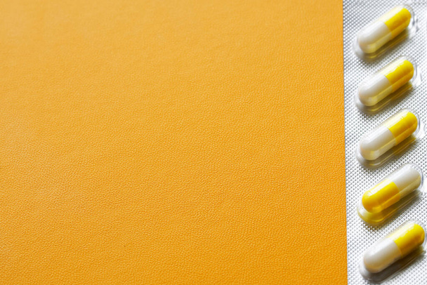 Желтые и белые медицинские капсулы в серебряных волдырях на желтом искусственном кожаном фоне. Концепция заполняемой формы. Свободное место для надписи. Селективное фокусирование. Макро - Фото, изображение