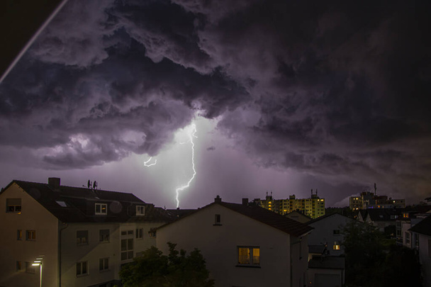 Изображение удара молнии по зданиям с угрожающими облаками в ночное время - Фото, изображение