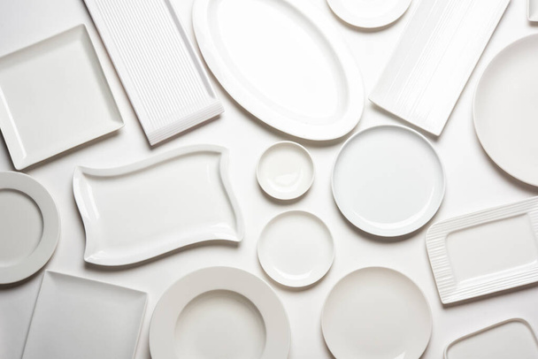 Placas vacías de cerámica blanca en grupo sobre fondo blanco, vista superior - Foto, Imagen