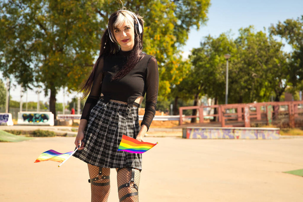 Χαριτωμένο νεαρό κορίτσι με κοτσίδες, λευκά ακουστικά και punk στυλ με γκέι σημαίες υπερηφάνεια. - Φωτογραφία, εικόνα
