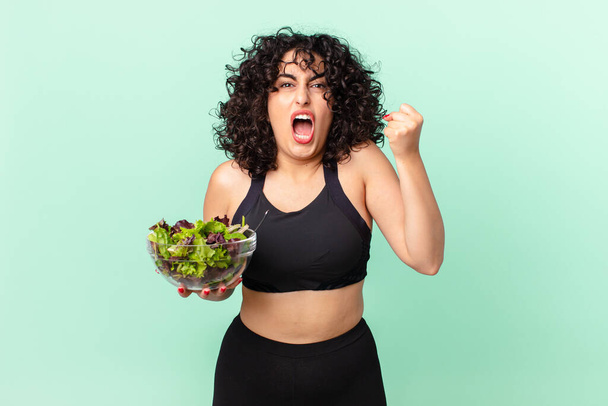 pretty arab woman shouting aggressively with an angry expression and holding a salad. diet concept - Foto, immagini