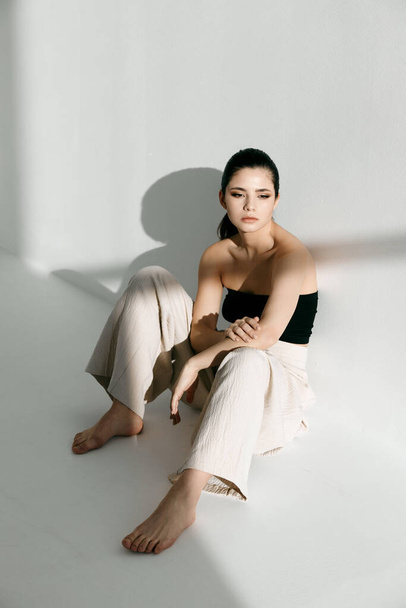 barefoot woman sitting on the floor indoors fashionable clothes bright light - Photo, Image