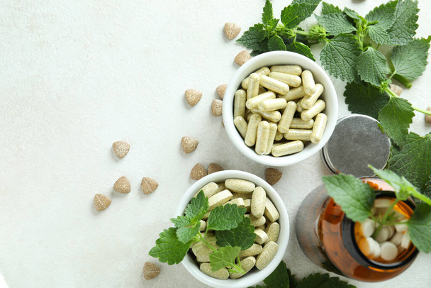 Píldoras e ingredientes de ortiga en mesa texturizada blanca - Foto, imagen