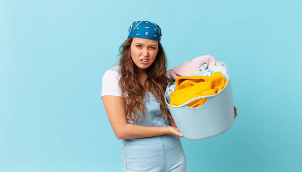 young pretty woman feeling puzzled and confused and holding a wash clothes basket - 写真・画像
