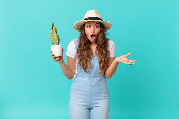young pretty woman amazed, shocked and astonished with an unbelievable surprise and holding a cactus - Photo, image
