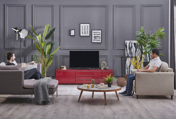 Dos hombres pasando tiempo en casa, fondo de pared gris decorativo y viendo el estilo de televisión. - Foto, Imagen