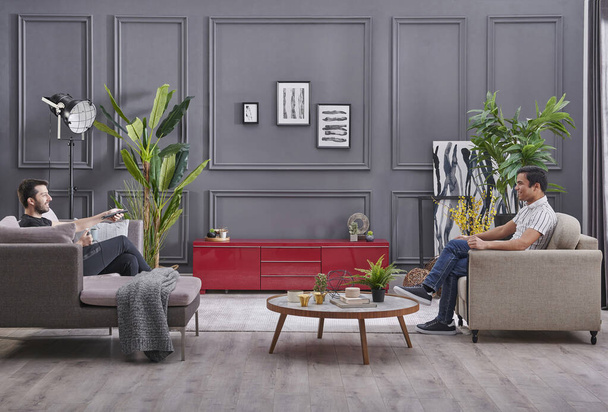 Двое мужчин проводят время дома, декоративный серый фон стены и смотреть телевизор стиль. - Фото, изображение