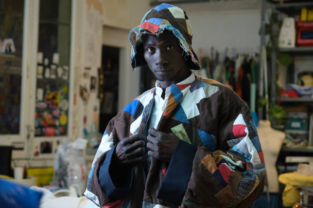 Porträt eines afrikanischen Mannes in traditioneller farbenfroher Kleidung und Hut in seiner Nähwerkstatt. - Foto, Bild