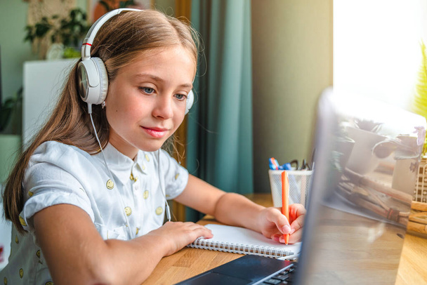 Gyönyörű kislány otthon tanul laptoppal, online e-learning rendszeren keresztül tanul - Fotó, kép