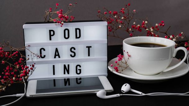 Podcasting lettering. Cuffie cellulare. Decorazione secca fiori rosa. Posto di lavoro. Caffè nero. Podcaster, podcast Audiolibri - Foto, immagini