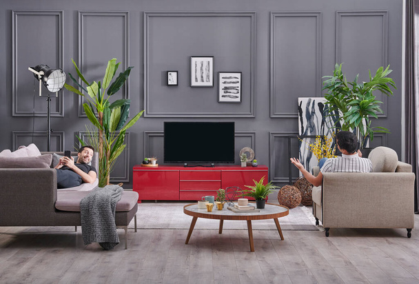 Két férfi időt tölt otthon, dekoratív szürke fal háttér és tévénézés stílus. - Fotó, kép