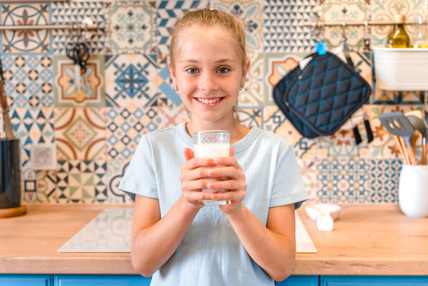 Una hermosa niña bebe un vaso de leche fresca en una cocina moderna de moda, el concepto de salud de los niños - Foto, imagen