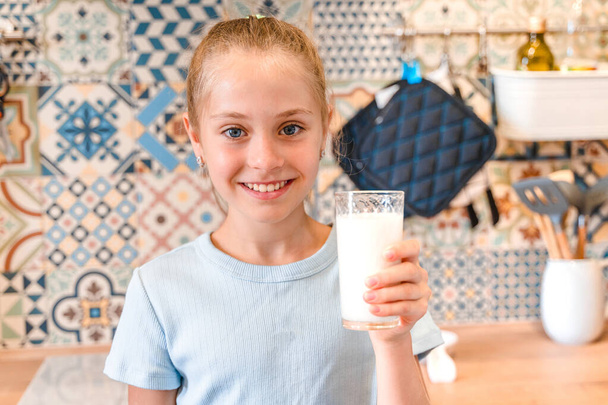 Krásná holčička pije sklenici čerstvého mléka v módní moderní kuchyni, dětský zdravotní koncept - Fotografie, Obrázek