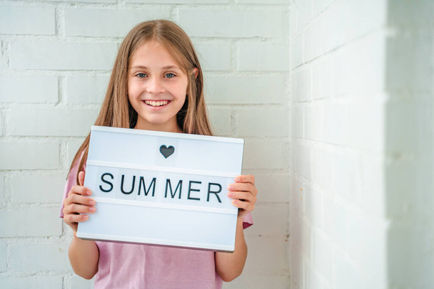 Una niña feliz sostiene una pancarta con la palabra "verano"" - Foto, Imagen