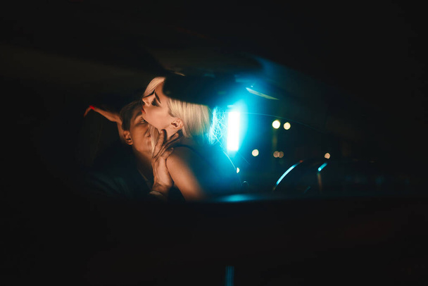 Egy pár csókolózik esténként a kocsiban. Gyengéd éjszakai fotózás a városban. Nyári vakáció szerelmeseknek. - Fotó, kép