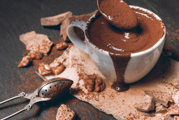 Domácí kořeněná horká čokoláda se skořicí v bílém porcelánovém kelímku na kamenném nebo betonovém pozadí - Fotografie, Obrázek