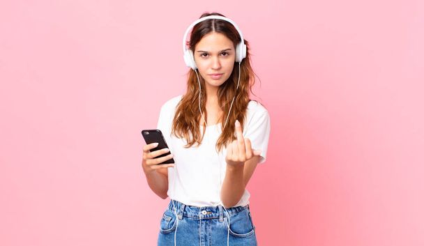 young pretty woman feeling angry, annoyed, rebellious and aggressive with headphones and a smartphone - Fotó, kép