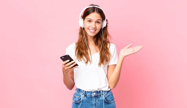 young pretty woman feeling happy, surprised realizing a solution or idea with headphones and a smartphone - Фото, изображение