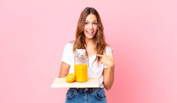 young pretty woman feeling happy and pointing to self with an excited and holding a tray with an orange juice - Foto, imagen